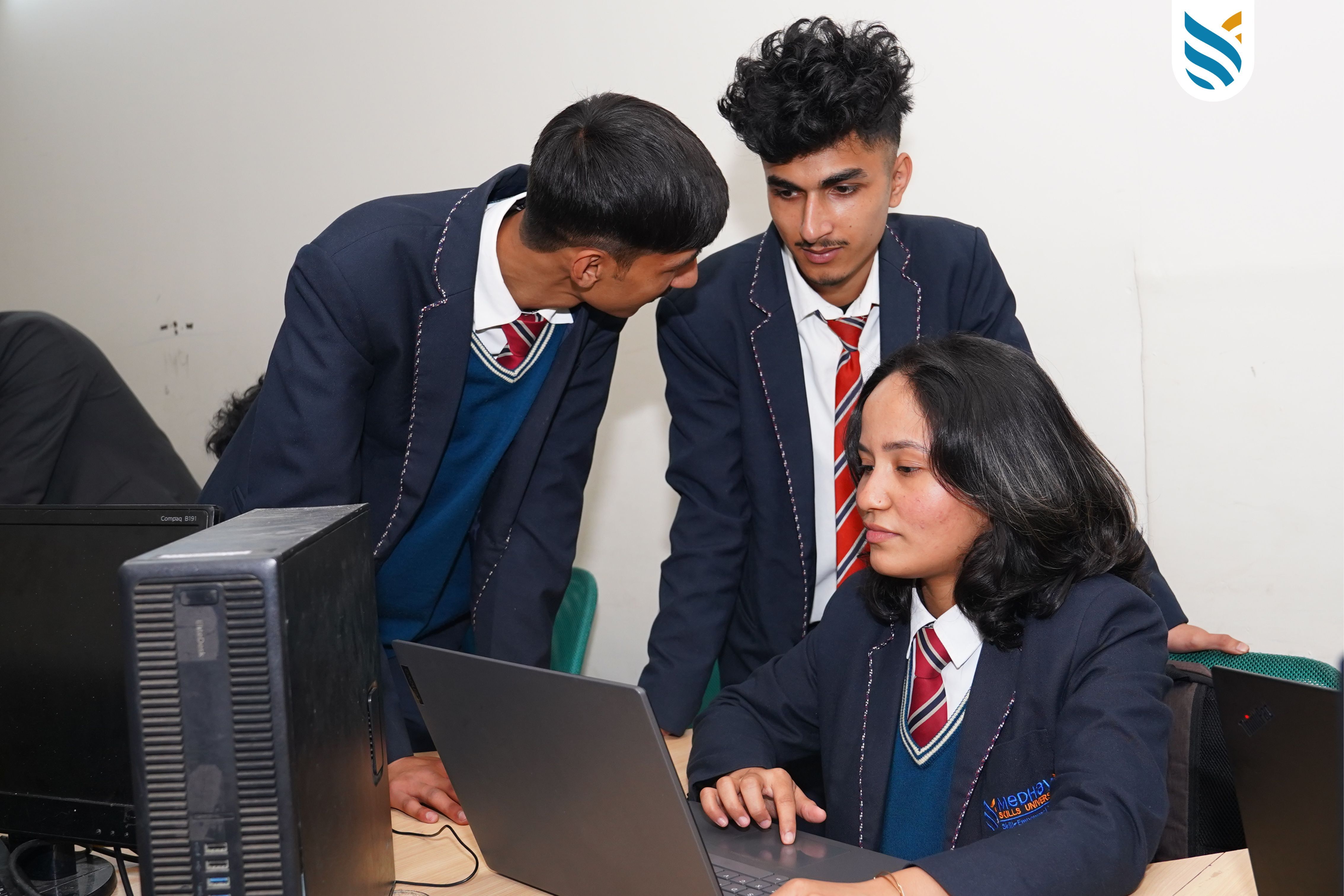 Three young men in school uniforms collaborate while looking at a laptop screen together.