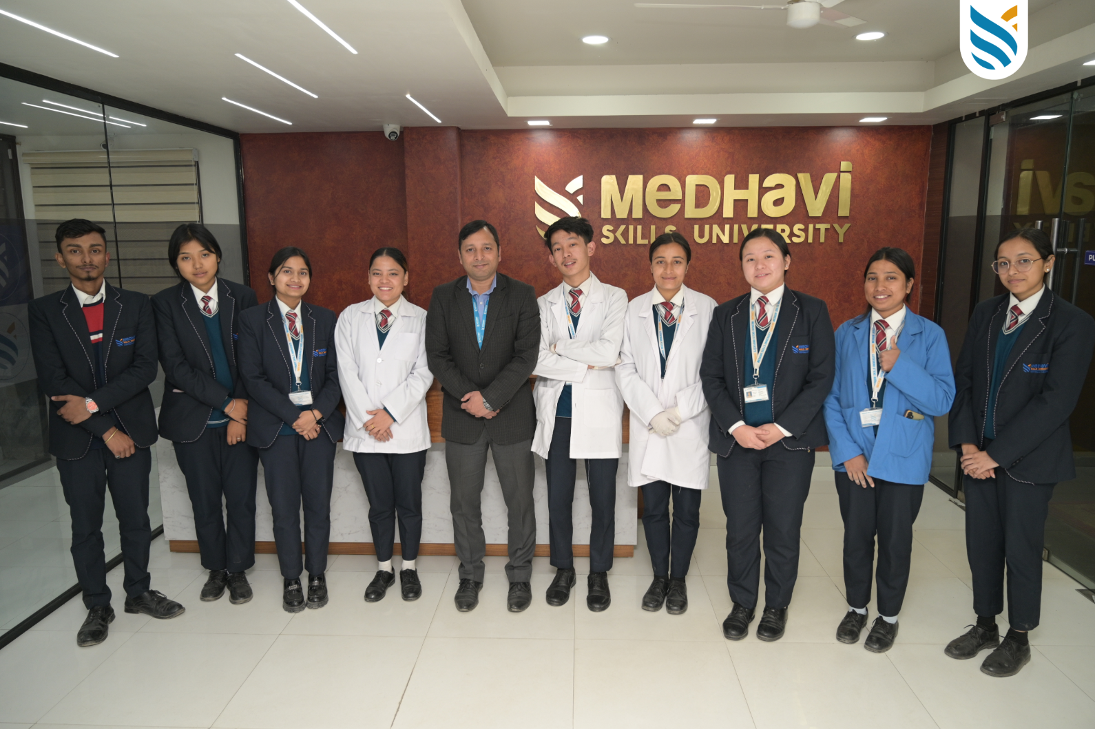 A group of students and a staff member stand in front of a "Medhavi Skills University" sign. They are dressed in formal attire and lab coats, smiling confidently, conveying a professional and positive tone.